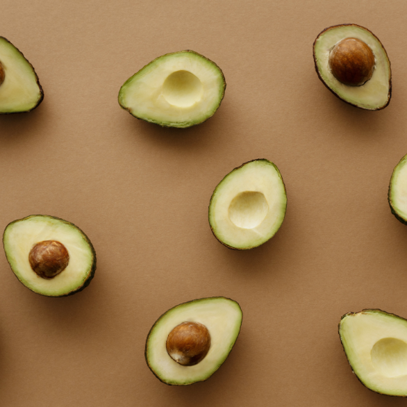 Aguacates abiertos, algunos con hueso y otros no, sobre una mesa marrón.