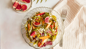 Ensalada de fruta en un plato transparente, sobre una mesa y con un tenedor a un lado.