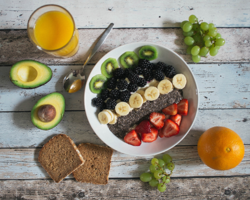Frutas en un bol sobre una mesa, aguacate sobre la mesa, uvas pan y un zumo de naranja.
