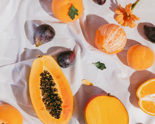 Una mesa repleta de frutas, higos, papayas, mandarinas peladas y flores narajanas.